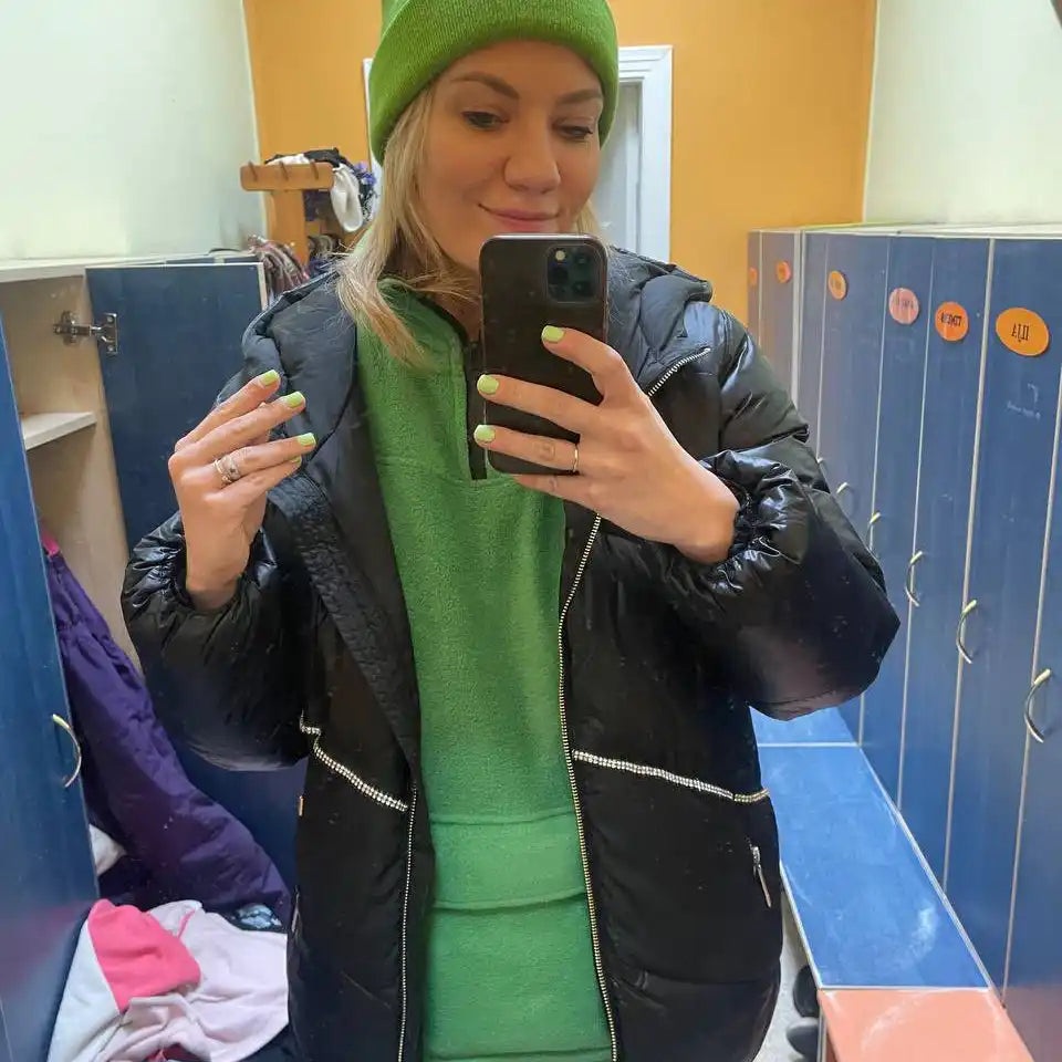 Woman in green hat and dress with black puffer jacket.